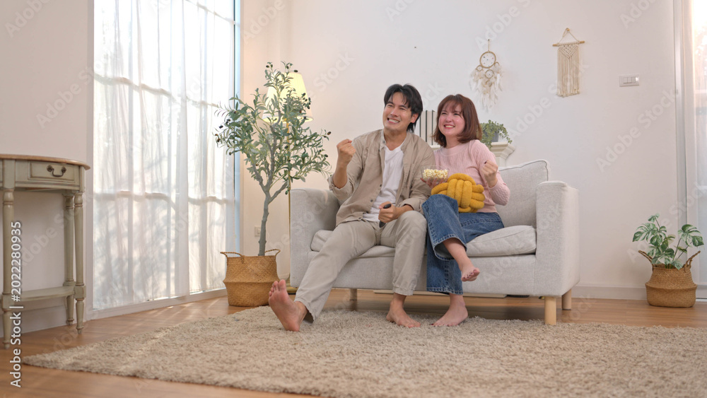 Obraz premium Excited young couple cheering on sofa while watching television