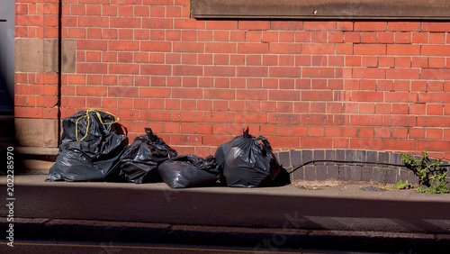 Foto Garbage bags on street, black trash sacks near brick wall, urban waste managemen