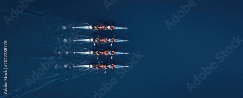 Synchronized rowing team paddles kayaks in unison across deep blue water. Athletes train together in race boats striving for speed and teamwork success.