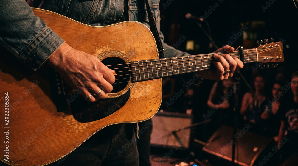 Obraz premium Acoustic Guitarist Playing on Stage with Audience in Background