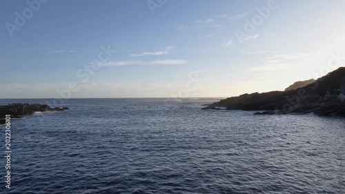 Moving shot across the suspension bridge at Storm’s River Mouth, Tsitsikamma National Park, South Africa, where ocean waters meet a rugged rocky shoreline showcasing the tranquil beauty at dusk.