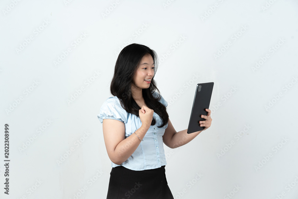 Naklejka premium Excited Asian woman holding a tablet showing winning expression on white background