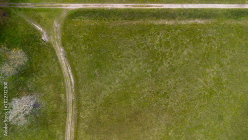 Obraz na płótnie Top down aerial view of a green meadow with a dirt path intersection and a lonely bench
