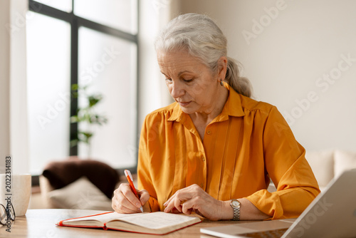 Photos Senior woman planning tasks in home office taking notes