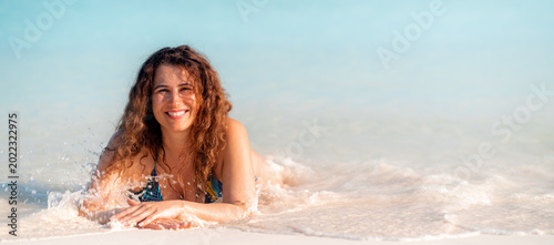 Foto A woman with dark hair relaxes on a white beach, wearing a blue swimsuit, gazing at the camera, enjoying a tropical holiday, serene