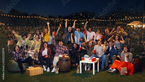 Konstfotografi Young crowd raising hands at night fan zone watch party