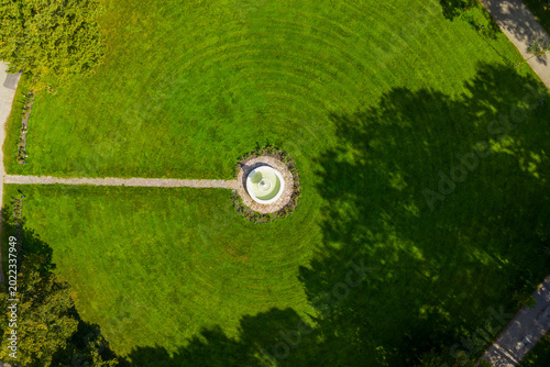 Aerial view of a circular stone fountain centered in a lush green lawn with concentric mowing patterns in Taujenai, Vilnius County, Lithuania.