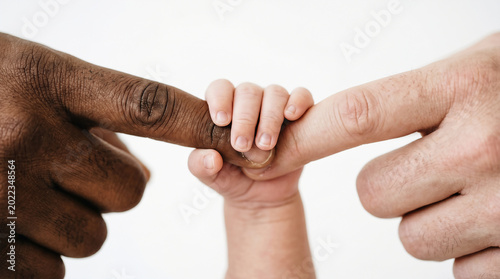 Inclusive Parent’s Day concept showing a baby holding two diverse parent fingers. Emotional macro image representing adoption, belonging, chosen family, and unconditional connection in PNG background