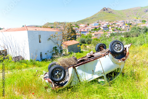 Upside down rusted car wreck in grassy field, Eresos village, Greece