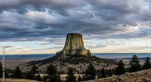 Devils Tower stands tall as a massive geological formation against a dramatic cloudy sky.