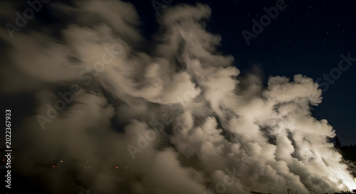 Steam billows from a geothermal power plant during a dark night in the wilderness.