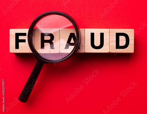 Magnifying Glass Examines Fraud Word on Red Background.