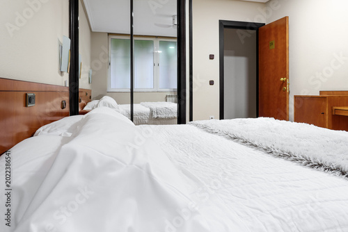 Hotel room interior with comfortable bed and mirrored wardrobe. 