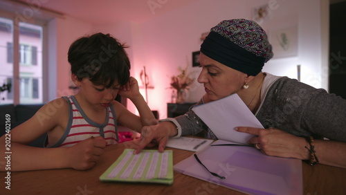 Фотография Mother undergoing chemotherapy helping child with homework at home, headscarf pa