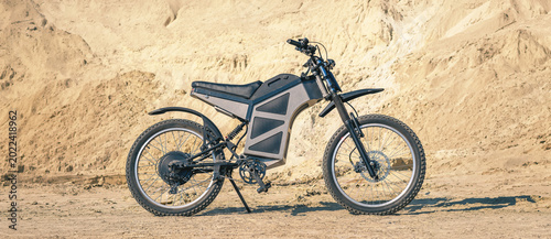 Powerful electric off road bicycle standing on sandy surface. Rugged tires and modern construction.