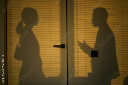 Photos Medium shot of young adult couple standing apart behind frosted glass, confronting separation and divorce conflict