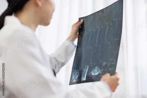 Fotografia Asian Female Doctor in White Coat Reviewing X-ray Image