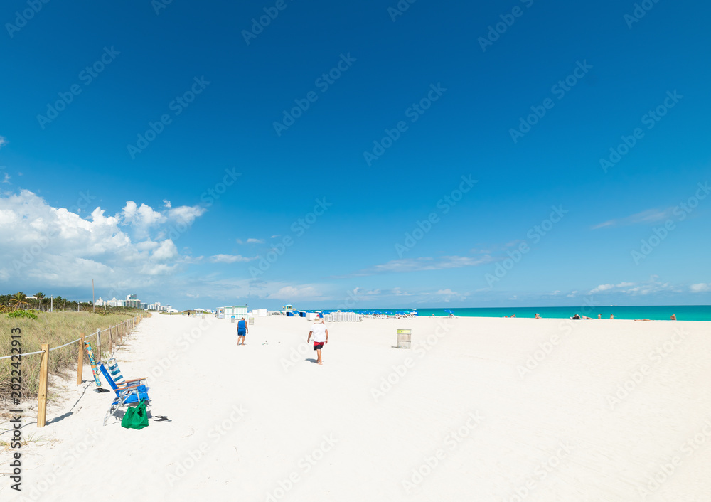 Fototapeta premium Beach chairs with beach bag and three men walking away on South Beach shoreline