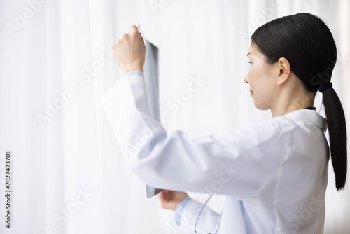 Fotografía Asian Female Doctor in White Coat Reviewing X-ray Image