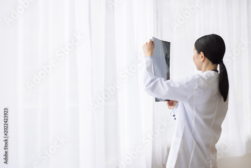 Fotografia Asian Female Doctor in White Coat Reviewing X-ray Image