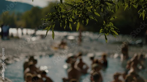 Crowd of vacationers at Malkinskiye hot springs with landscaped area and with bridge over river and parking lot for cars near mountain