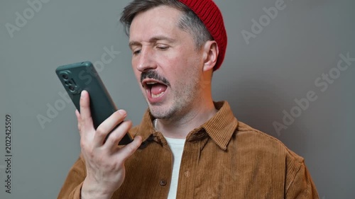 A man in his 30s with light skin and a mustache is using a smartphone while standing in an indoor location. The man can't hear the ringing bell, can't get through, problems with his mobile phone