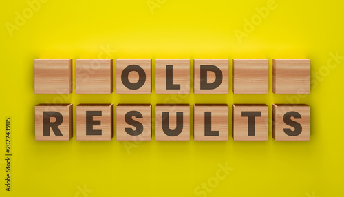 Fotografie Old Results Word Blocks on Yellow Background: Wooden blocks displaying OLD RESULTS against a vibrant yellow backdrop, symbolizing outdated information or past outcomes