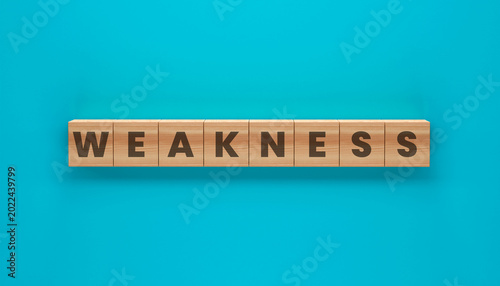 Photos Weakness in Wooden Blocks: Weakness spelled out on wooden blocks, set against a vibrant turquoise backdrop
