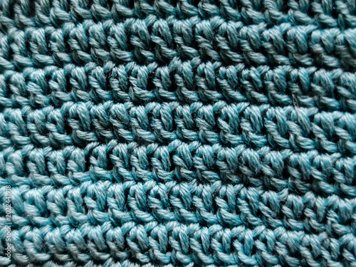Close-up macro of turquoise knitted fabric texture, handmade yarn pattern with soft loops and detailed textile structure.