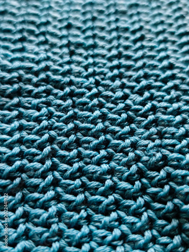 Close-up macro of turquoise knitted fabric texture, handmade yarn pattern with soft loops and detailed textile structure