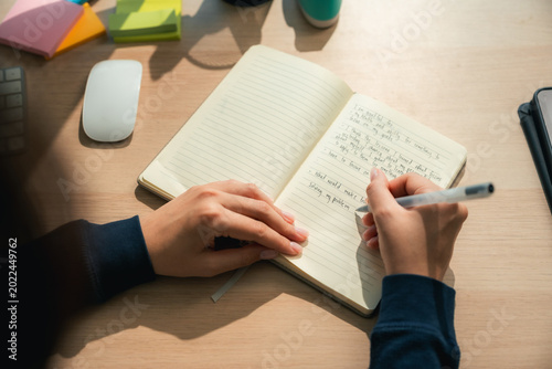 Fényképezés Modern Asian woman sitting in a cozy room, thoughtfully journaling in her notebo