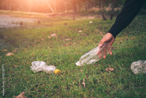 Hand person collecting plastic bottles in the lawn to keep it clean.