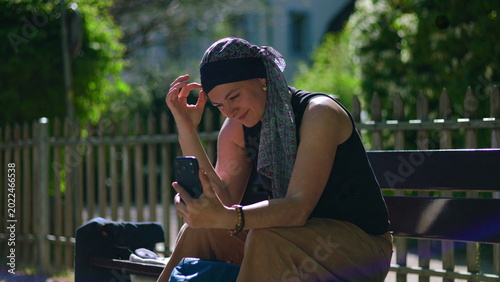 Billede på lærred Woman undergoing chemotherapy sitting on park bench during video call, listening