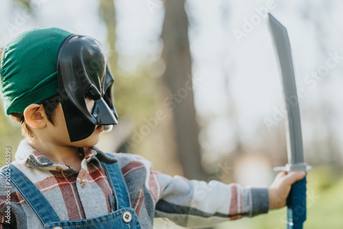 Foto Young child wearing a black superhero mask holds a toy sword outdoors