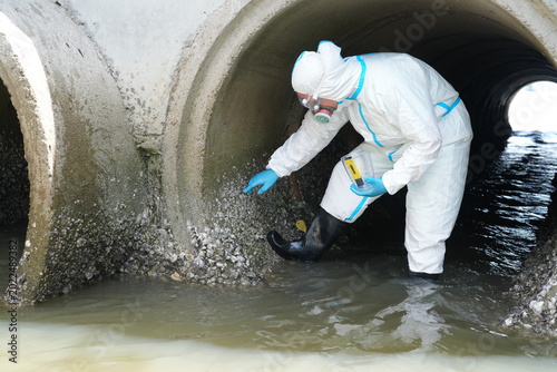 Obraz na plátně Environmental scientists wearing PE chemical protective suits stood in a tunnel collected water samples from a canal to check water quality after wastewater was treated and discharged into the sea