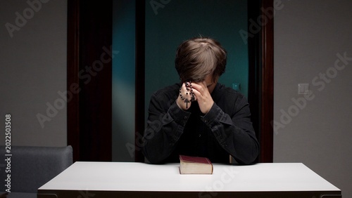 Foto Man with head bowed and hands clasped holding a rosary beside an antique bible o