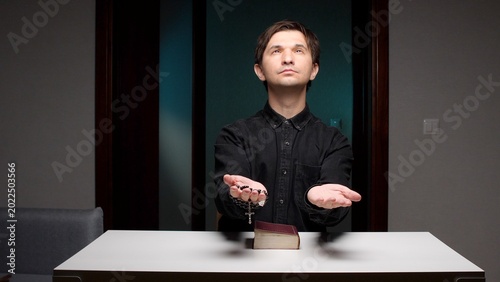 Canvastavla Young man sitting at a table looking up in prayer, holding a rosary in one hand