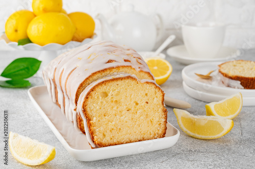 Lemon loaf cake with sugar icing on a white plate on a stone background. Copy space.