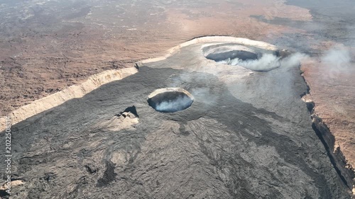 Aerial view of active volcanic craters with smoke rising from the dark basaltic lava fields in the Danakil Desert, Dallol, Afar, Ethiopia.