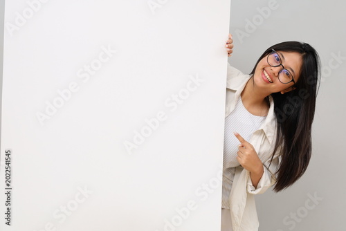 Portrait of a happy and excited young woman, smiling positively, pointing with finger, empty space, plain white billboard, advice, choice, isolated on white background.
