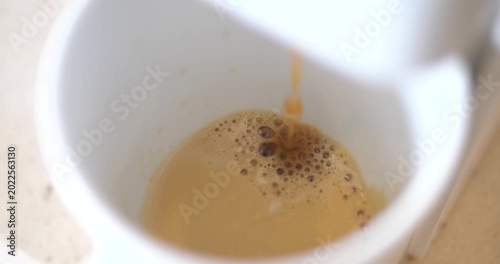 Cinematic top view of fresh hot espresso coffee extracting and dripping into a white ceramic cup, golden crema bubble texture close-up