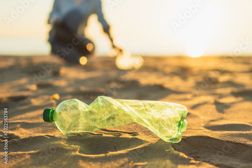 Bild auf Leinwand Green plastic bottle polluting sandy beach during sunset, highlighting global en