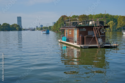 Obraz na plátně Wooden houseboats on spree river, with trees and the city of Berlin in the background
