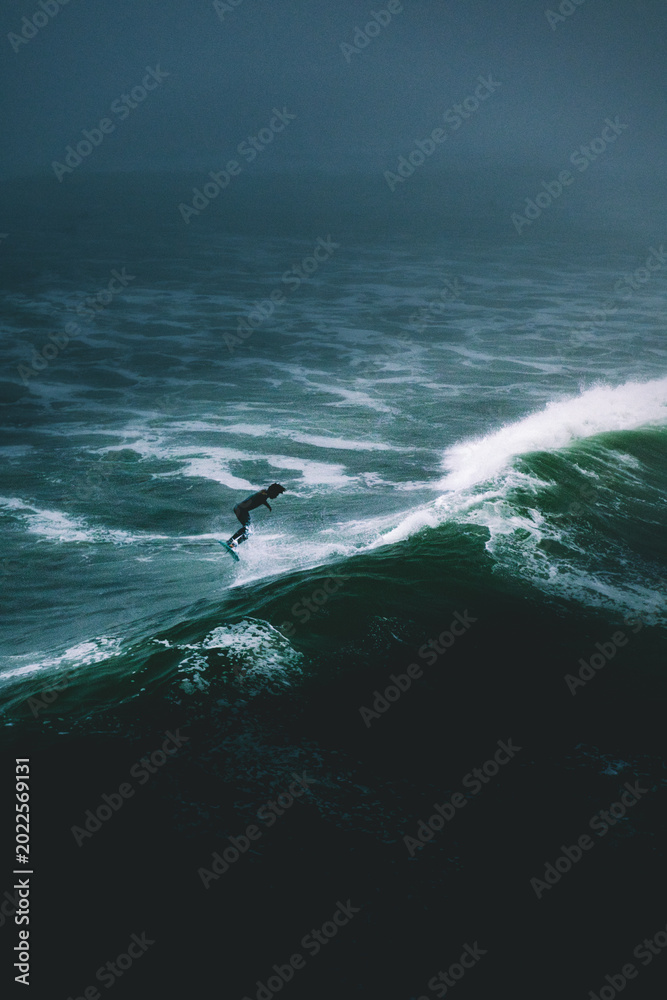 Obraz premium Lone Surfer Riding Dark Stormy Ocean Wave in Dramatic Aerial View