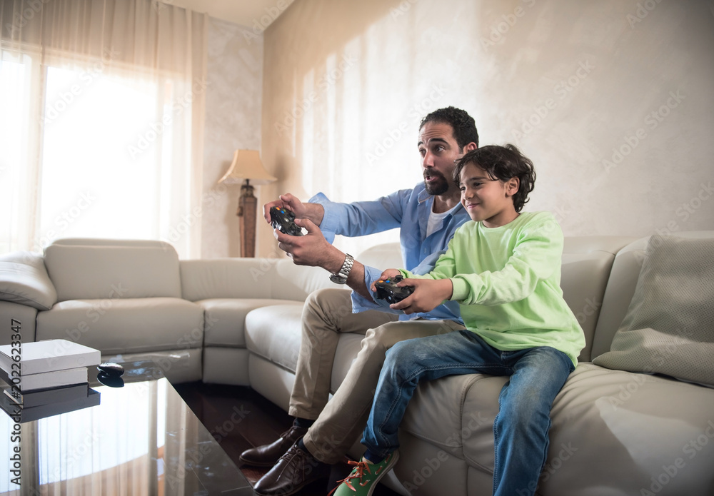 Obraz premium Modern Middle Eastern father and son playing video games together in bright living room