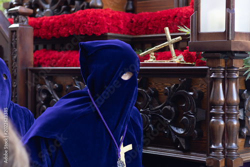 Foto Close-up of a penitent in a blue velvet robe and hood during a Holy Week procession, religious float with red carnations in the background, Asturias