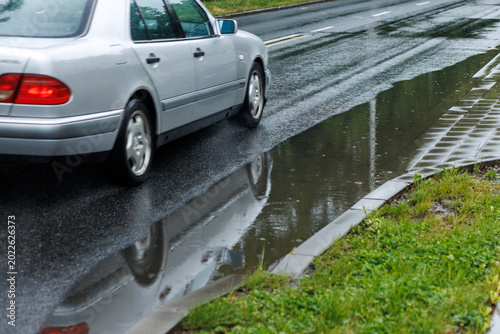 Car driving along wet road with large rain puddle