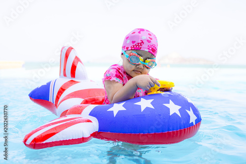 Cute Asian toddler girl playing with airplane inflatable float in luxury swimming pool next to the beach, summer vacation concept,A lovely little Asian child wearing a pink swim cap and goggles,