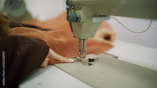 Close up of a person guiding brown sheer fabric under the needle of an industrial sewing machine