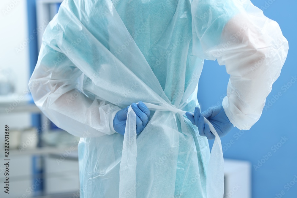 Fototapeta premium Medical worker tying disposable isolation gown indoors, closeup